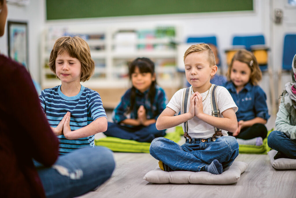 Kinder in der Schule, sitzen auf Kissen im Meditationssitz mit geschlossenen Augen
