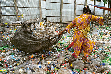 Asien, eine Person steht auf einem Berg von Müll und zieht einen Sack voll Plastik weg