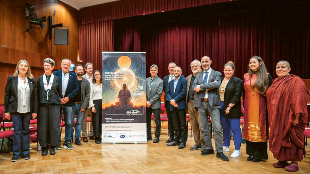 Im Konferenzsaal stehen Menschen links und rechts von dem Plakat mit dem die Konferenz angekündigt wurde. Die ungefähr 10 Menschen schauen in die Kamera.
