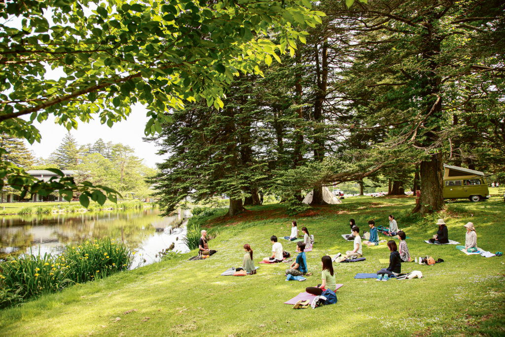 Muho in Karuizawa, im Garten des Prince Hotel. Er sitzt auf der Wiese am Fluss. Ihm gegenüber sitzen ungefähr 15 Personen im Schneidersitz unter Bäumen.