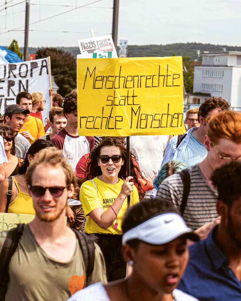 Protestierende westliche Menschen mit gelbem Plakat "Menschenrechte statt rechte Menschen" 