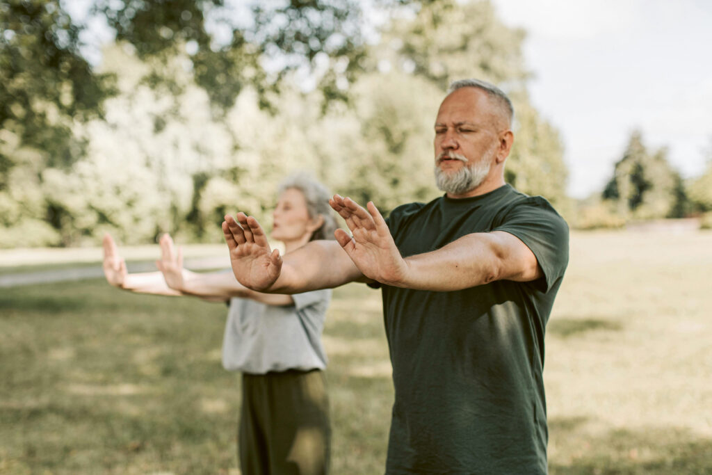 Mann und Frau in der Natur strecken ihre Hände mit den Handflächen aufgestellt nach vorne. Die Auge sind geschlossen