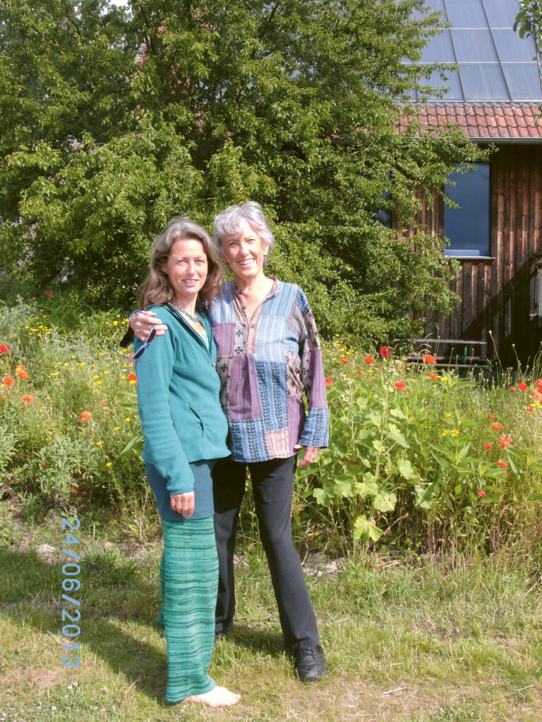 Joanna Macy und Gabi Bott vor Wiese Baum und Holzhaus