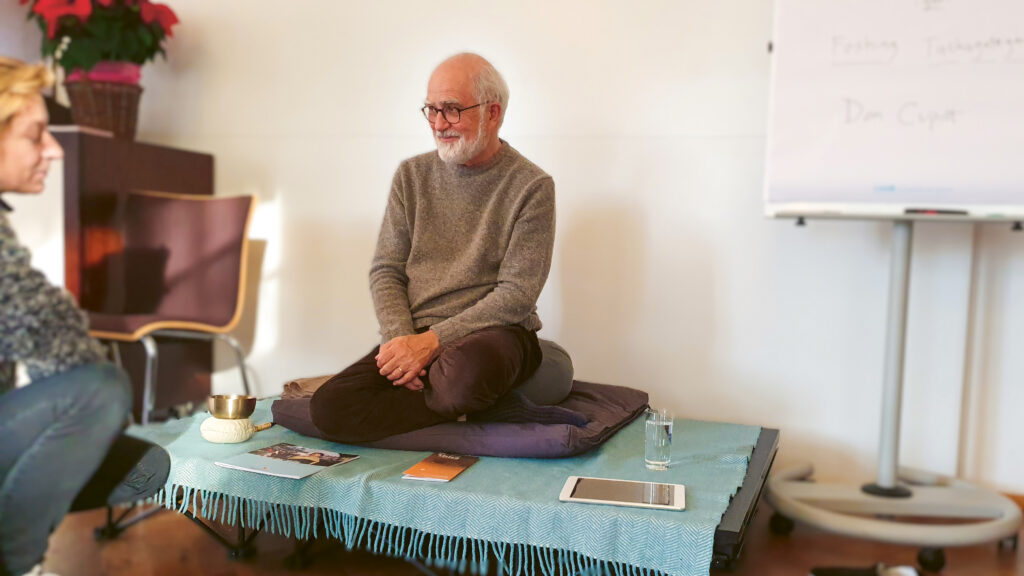 City-Retreat mit Stephen Batchelor. Er sitzt im Schneidersitz auf einem niedrigen Podest.